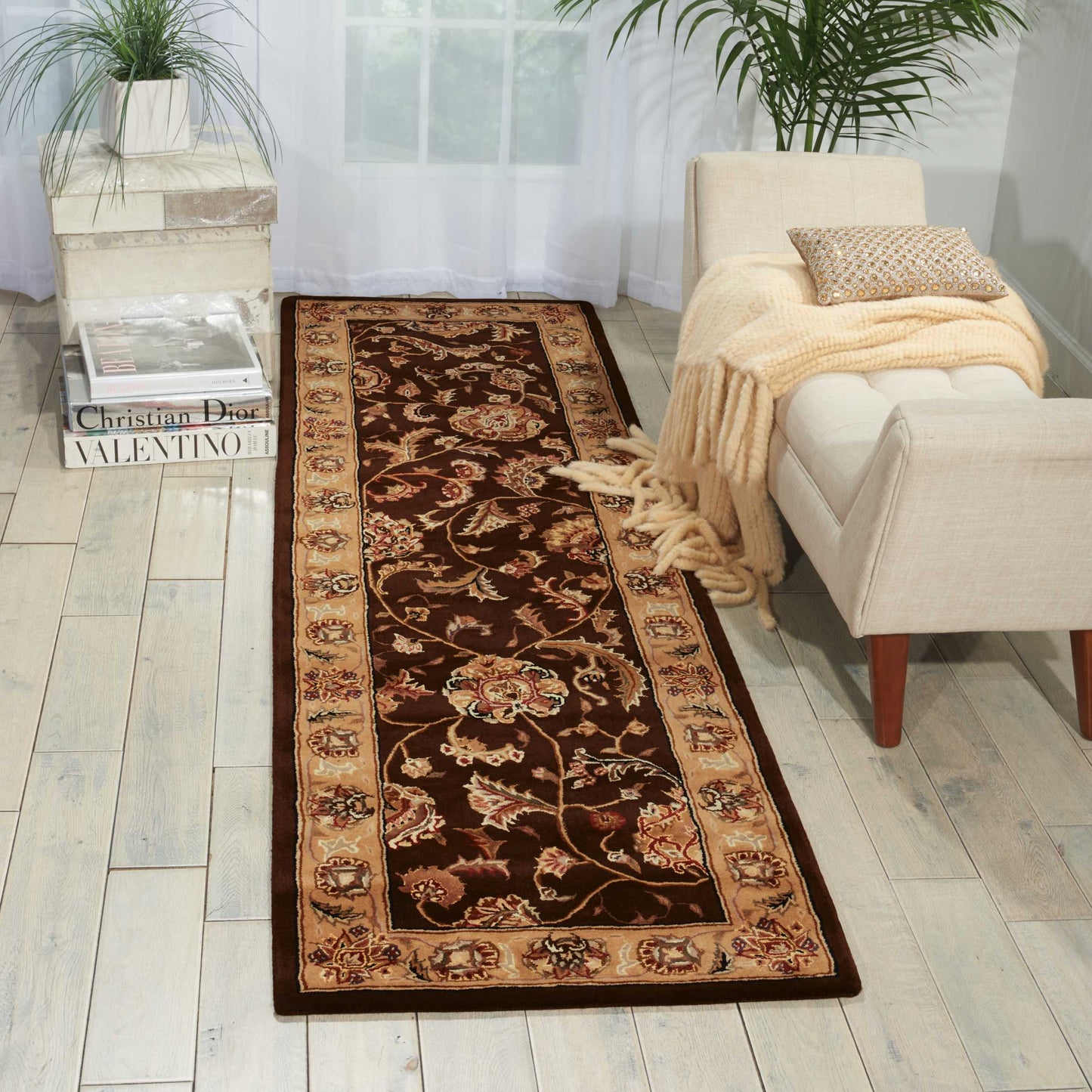 Long brown oriental runner rug with cream floral border, laid in a bright living room beside a beige sofa with a throw.