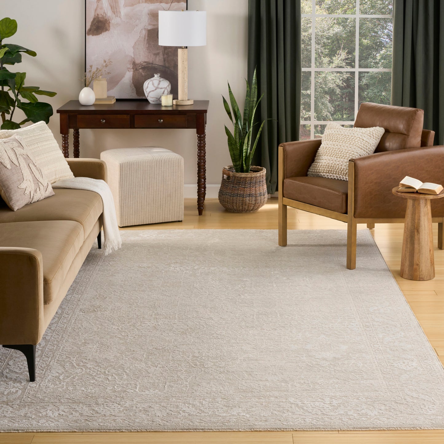 Cozy living room featuring a light gray rug sized 5' x 8', beige fabric sofa, brown leather chair, wooden tables, plants and green curtains.
