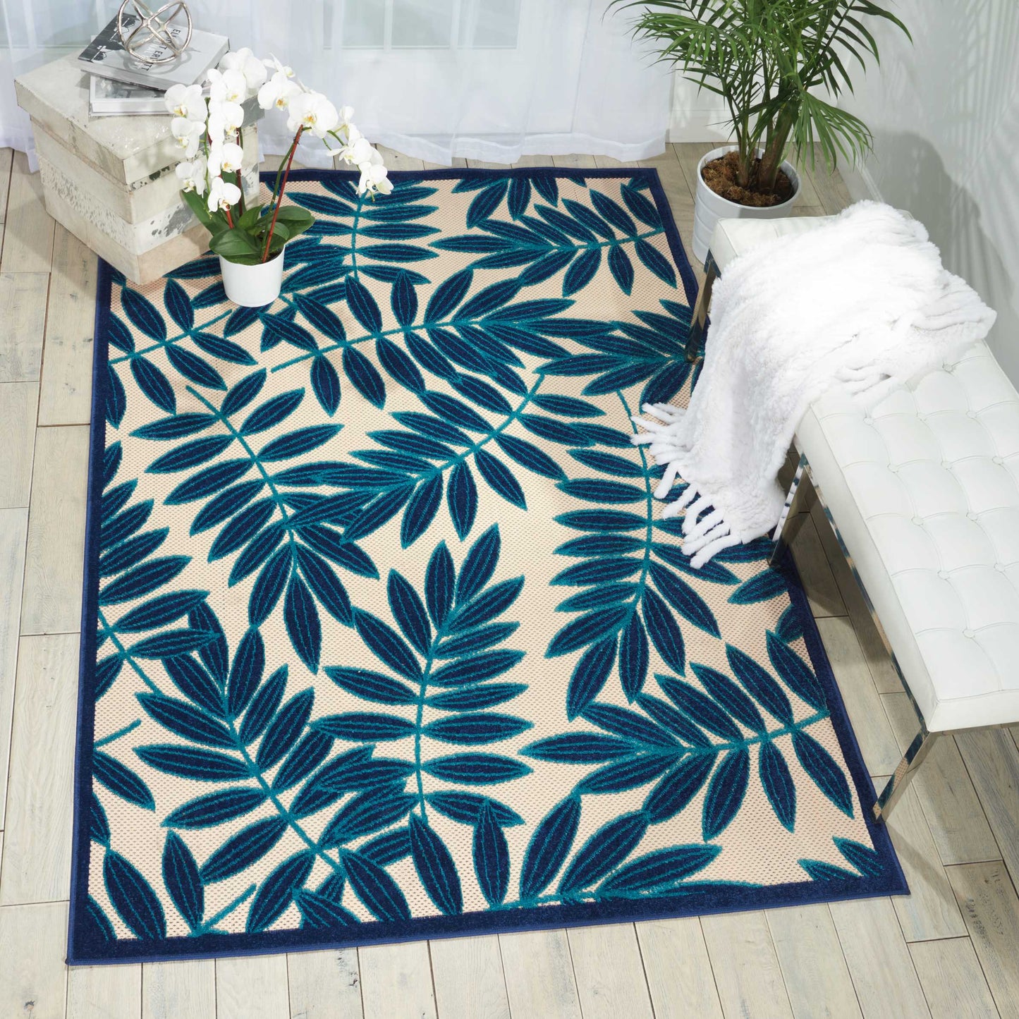 Rectangular area rug featuring a bold blue tropical leaf pattern with a navy border on beige.
