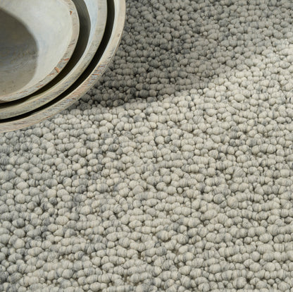 Close-up of a light gray loop-pile carpet with dense, tufted texture; cozy, modern rug for living spaces.