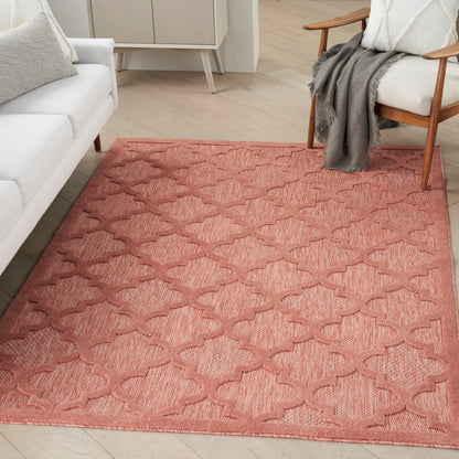 Rectangular coral-pink woven area rug with interlocking geometric pattern in a modern living room.
