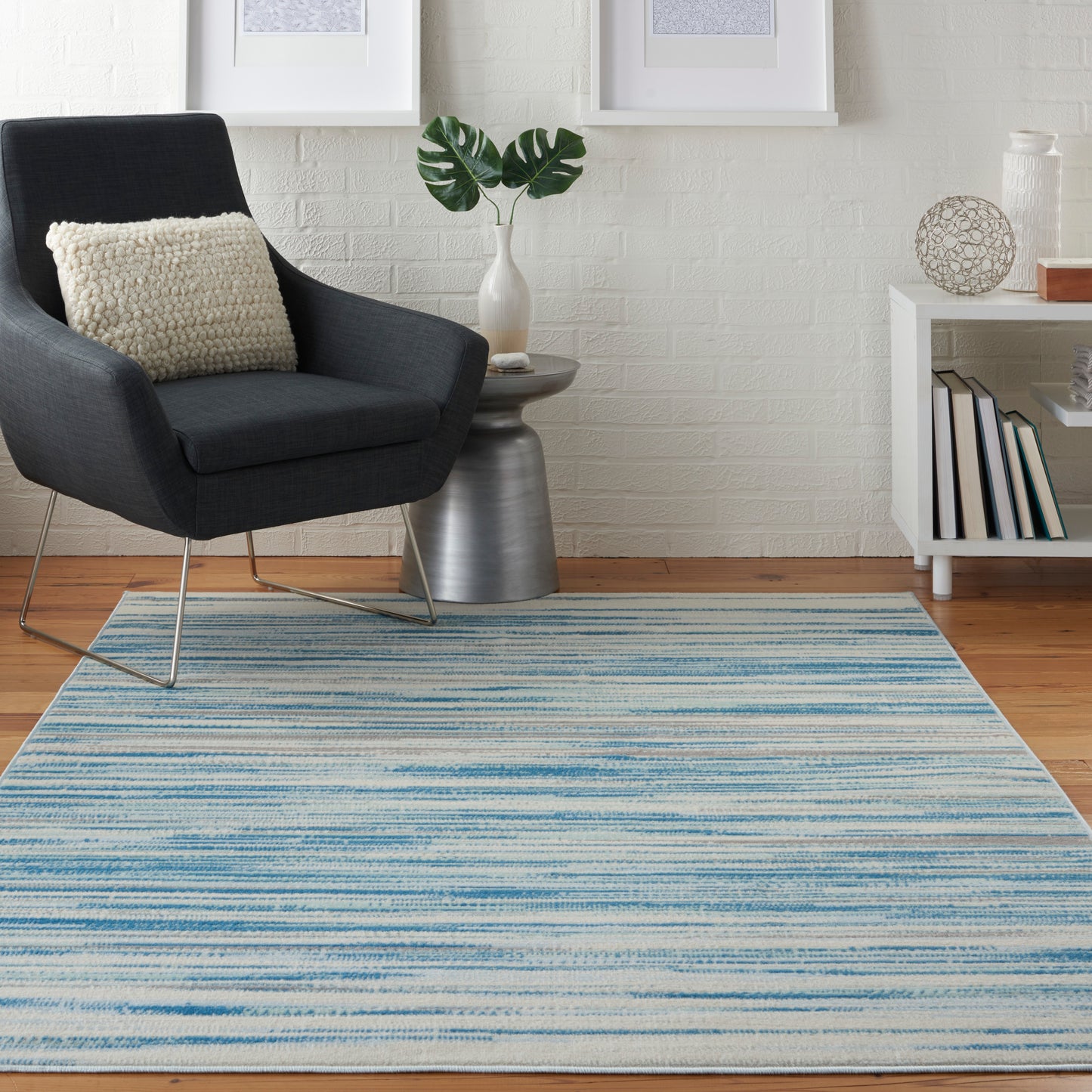 Modern living room with blue striped rug, dark gray armchair, cream textured cushion, white brick wall and white side table.