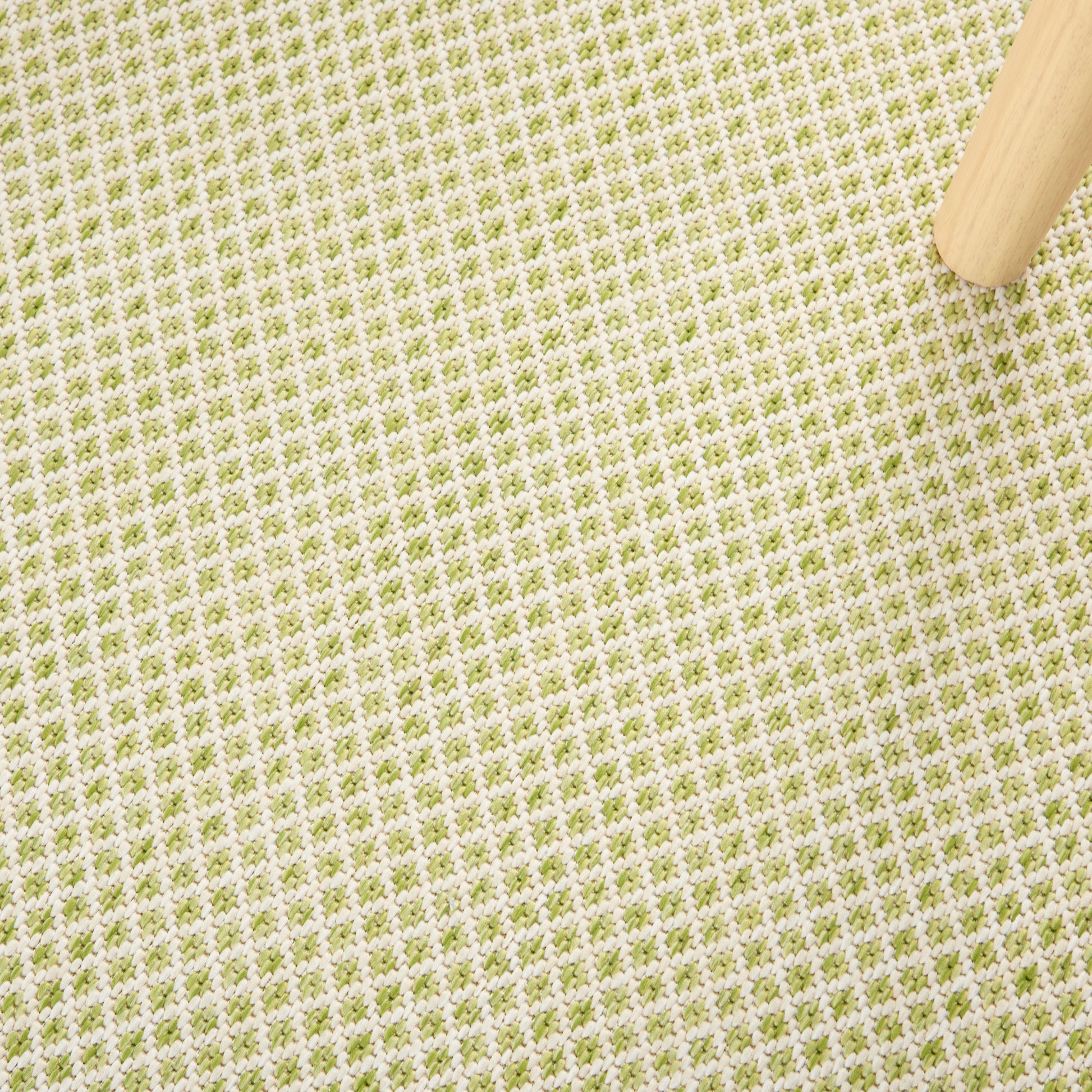 Beige woven fabric with small olive-green grid pattern; light wood leg in top-right corner.