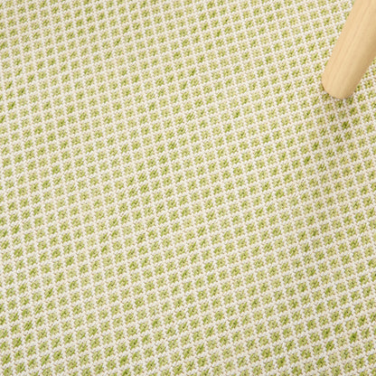 Beige woven fabric with small olive-green grid pattern; light wood leg in top-right corner.