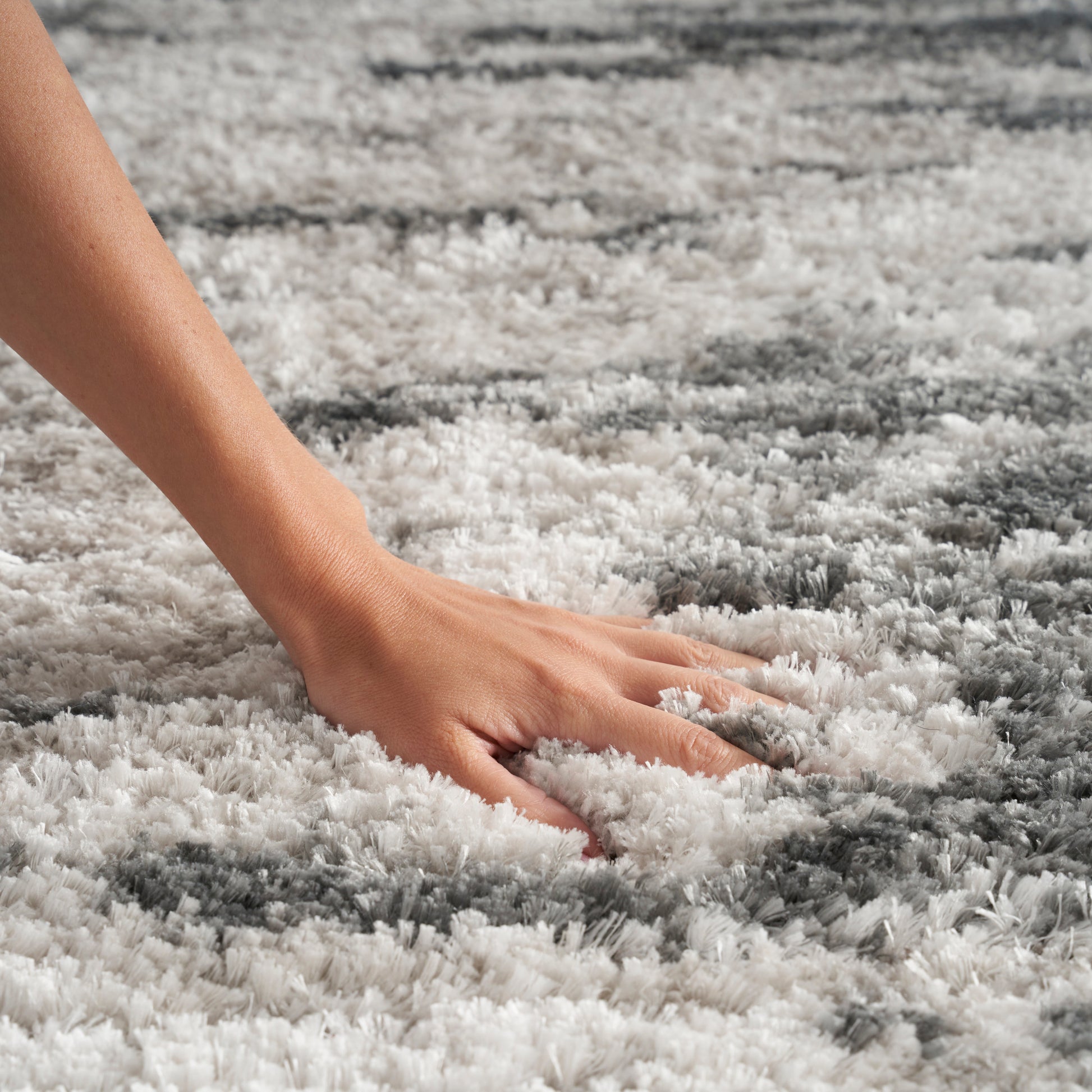 Close-up of a hand pressing into a plush white & gray shag rug with soft fluffy fibers.