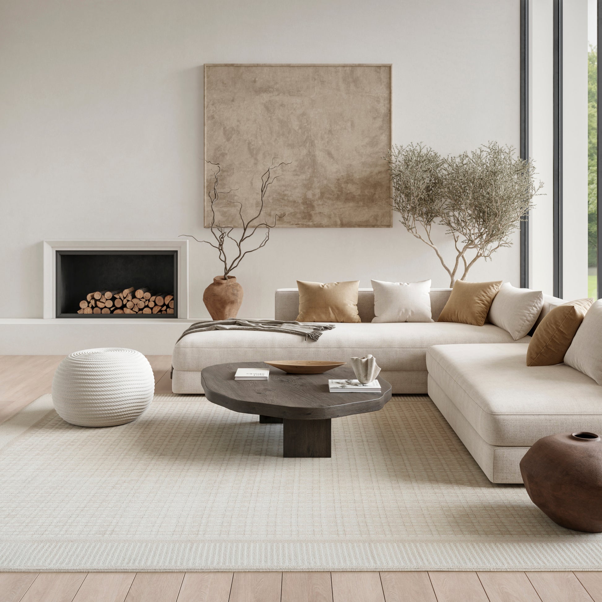 Neutral living room with beige sectional, dark round coffee table, white pouf, light rug, fireplace, and potted trees.