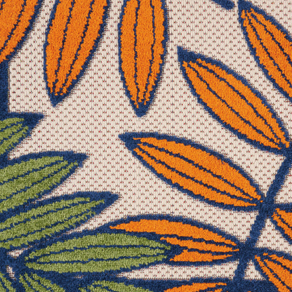 Close-up of rug fabric with orange & blue leaf shapes, green leaves, and a beige background in a bold tropical botanical pattern.
