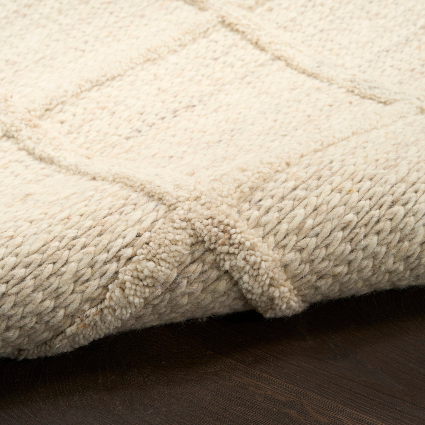 Cream plush rug with thick pile and geometric square pattern on dark wood floor.