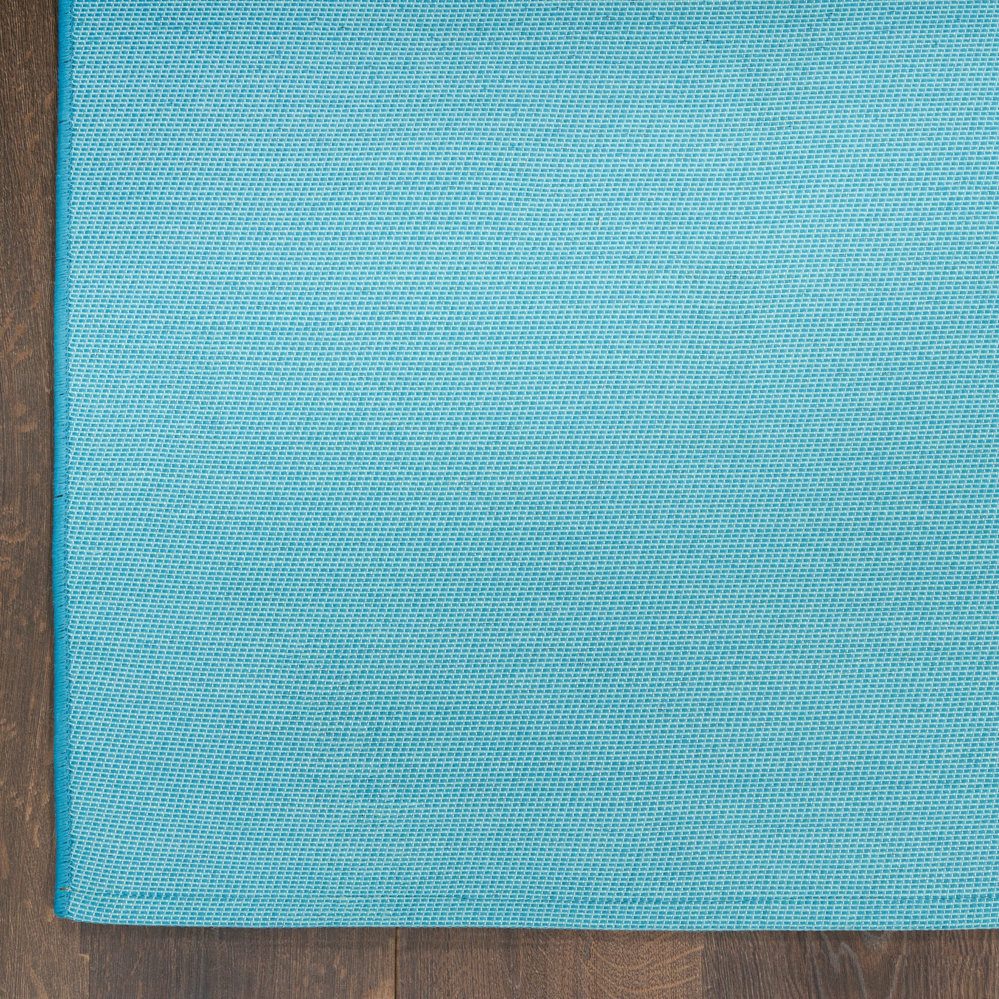 Teal woven fabric mat with fine grid texture, rectangular rug on dark wooden floor.