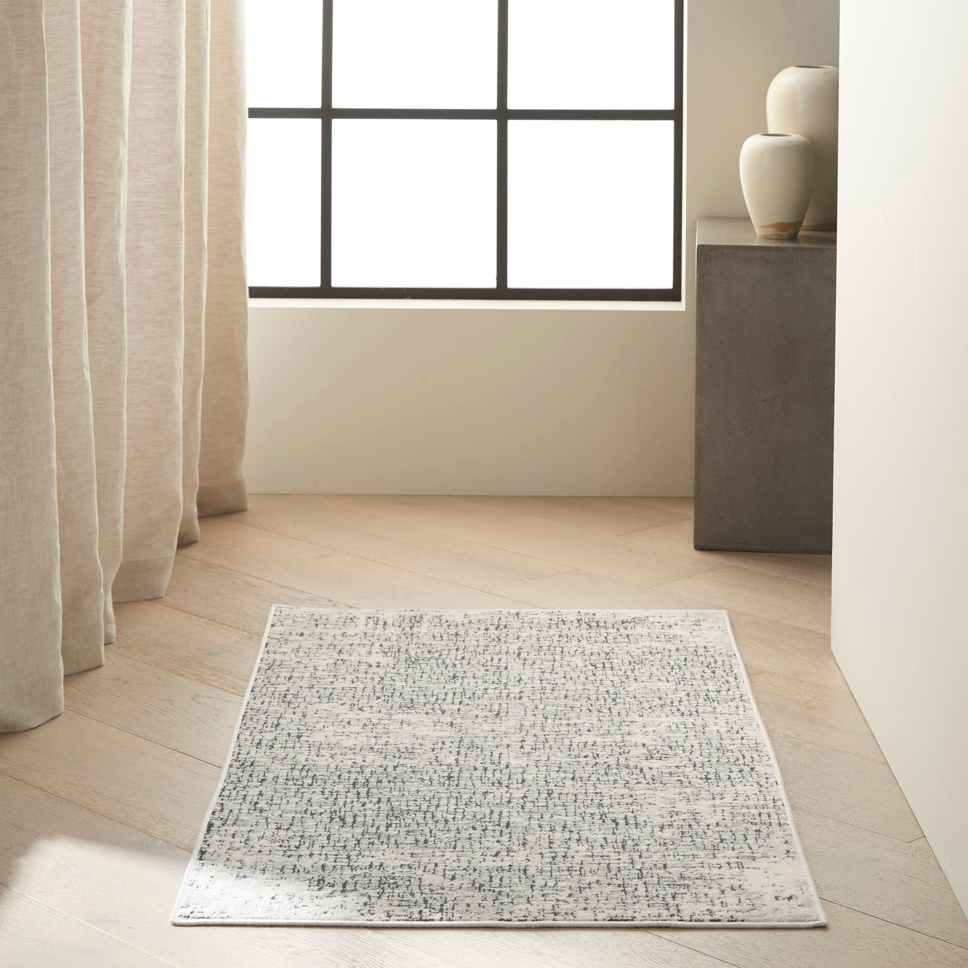 Rectangular grey and white abstract-pattern rug, low-pile, laid on light wood floor in a bright minimalist living room.