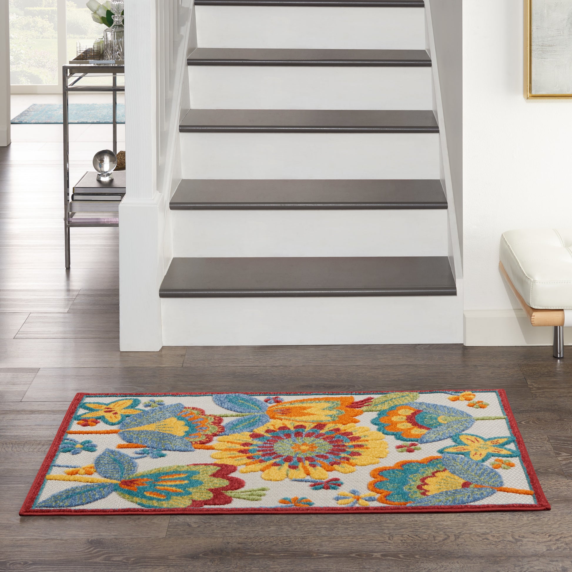 Rectangular floral area rug with orange, yellow, blue blooms & red border at the base of a staircase in a living room.