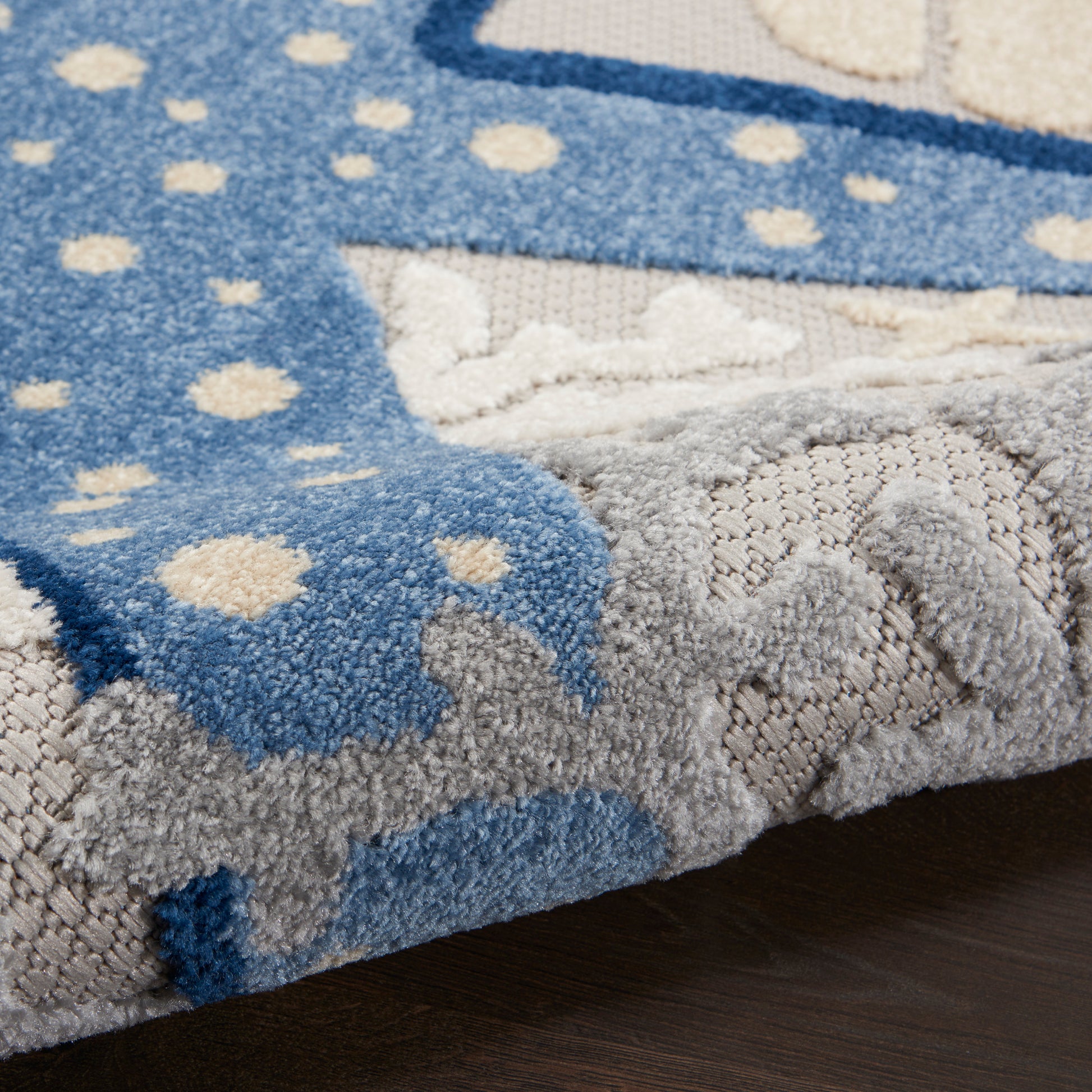Close-up of a plush blue and gray rug with white polka dots and abstract border; thick pile.