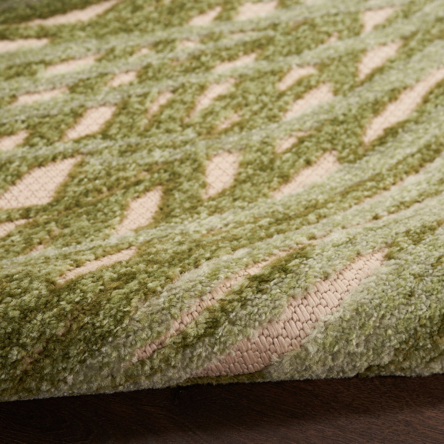 Close-up of a plush green rug with cream geometric pattern on a wooden floor.