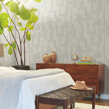 Modern Tribal wallpaper by Nikki Chu featuring a soft grey textured background with bold geometric tribal patterns in steel-blue tones. A contemporary non-woven wallcovering designed for modern interiors, accent walls, bedrooms, living rooms, and office spaces with a stylish artistic and textured finish.
