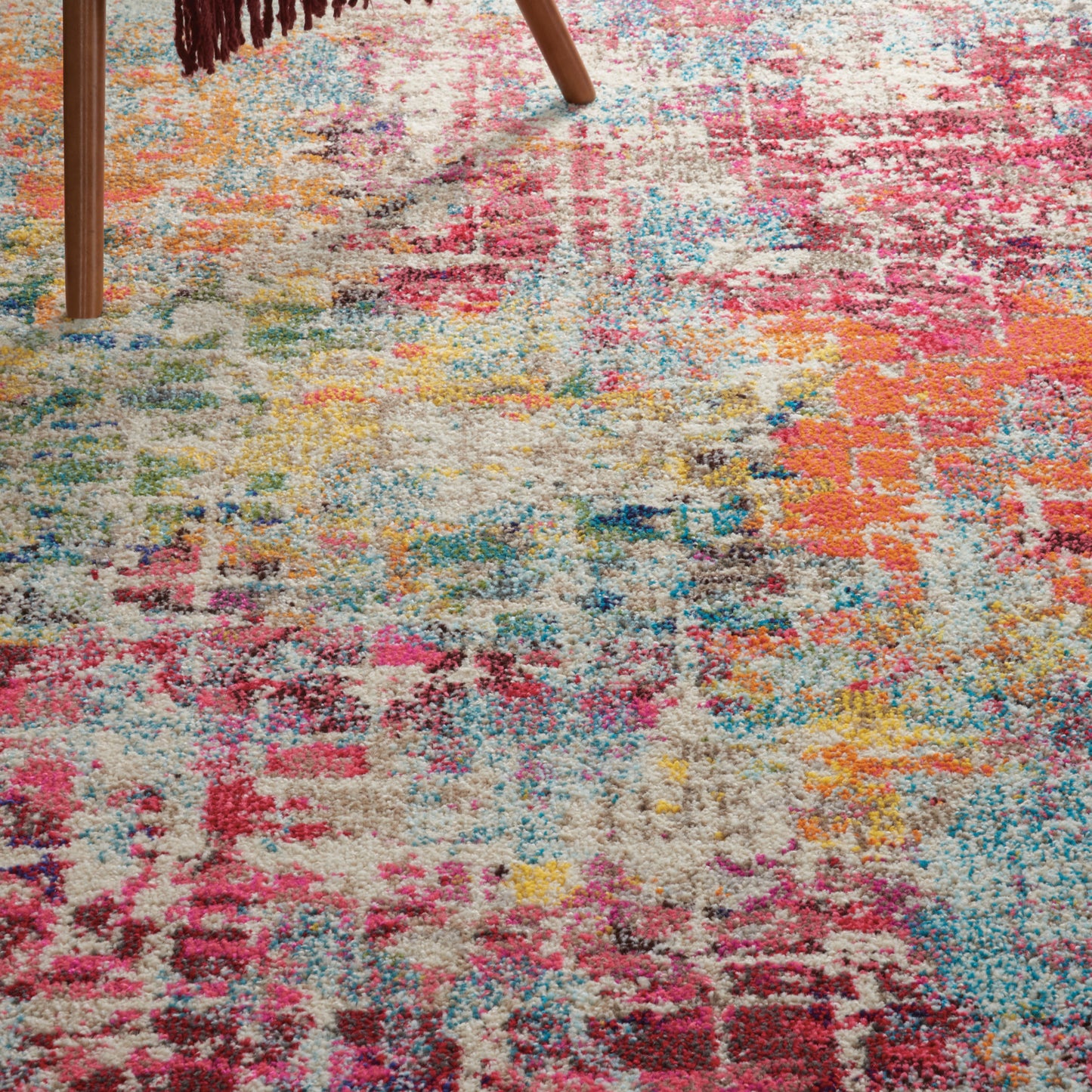 Colorful shaggy area rug with patchwork pattern in pink, orange, blue, yellow and beige; wooden chair leg nearby.