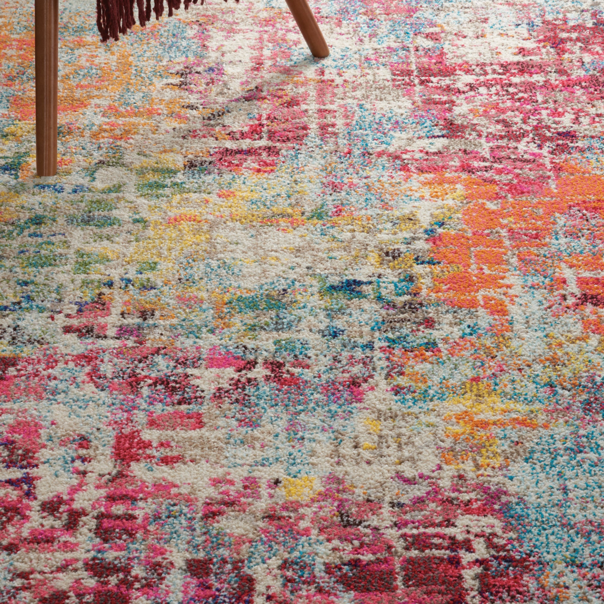 Colorful shaggy area rug with patchwork pattern in pink, orange, blue, yellow and beige; wooden chair leg nearby.