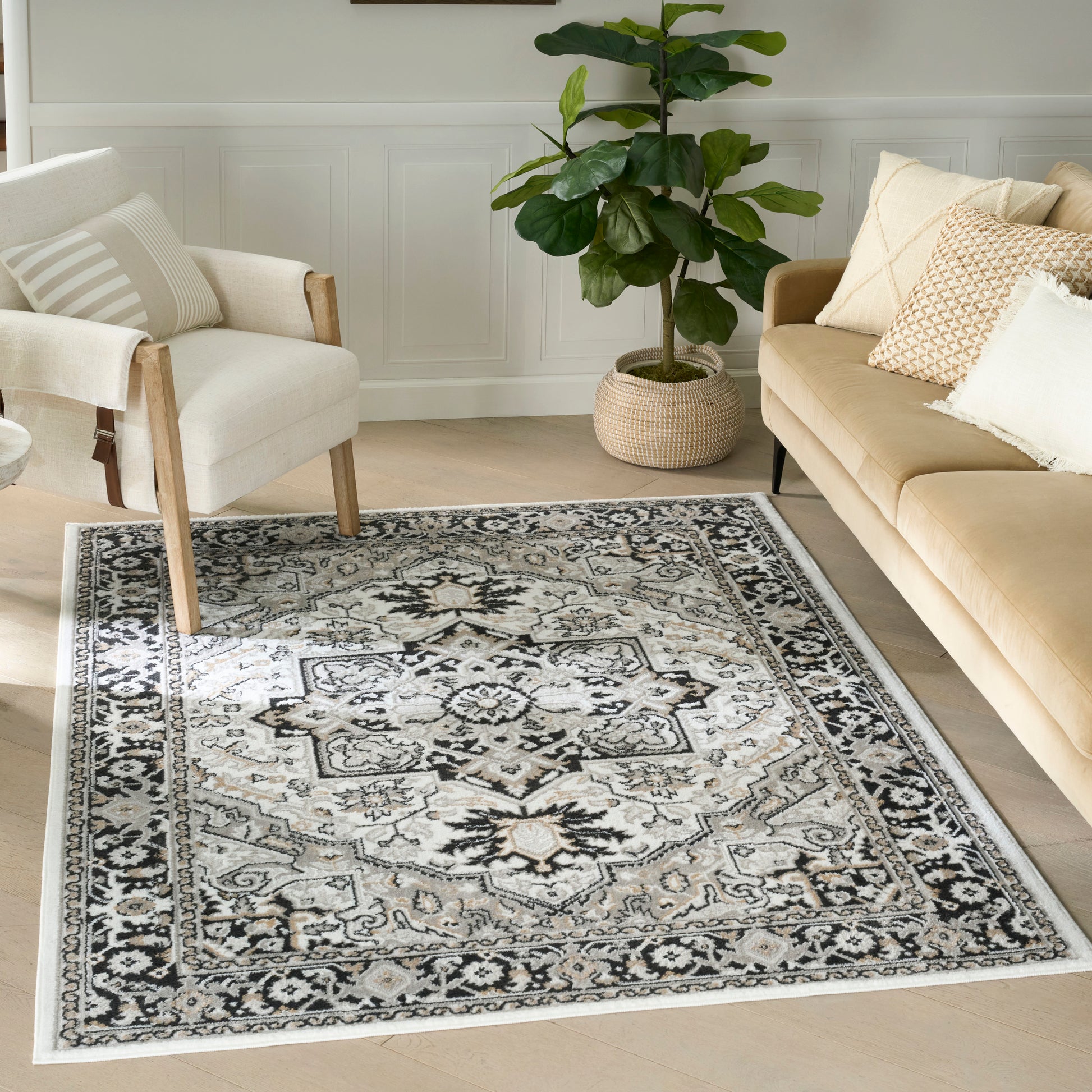 Neutral-toned area rug with central medallion and ornate border on light wood floor, with cream sofa, armchair and plant.