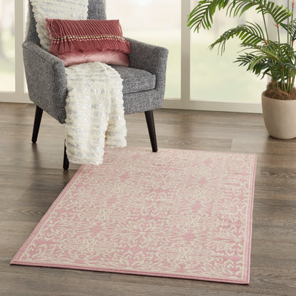 Pink floral-pattern rug on wood floor beside a gray mid-century chair with white throw and pink cushion, near a potted plant.