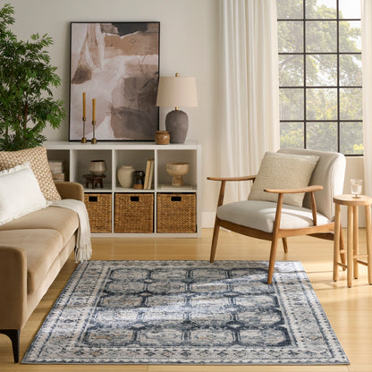 Cozy living room with blue-gray geometric rug, mid-century chair, beige sofa, wicker baskets, abstract art, and green plant.