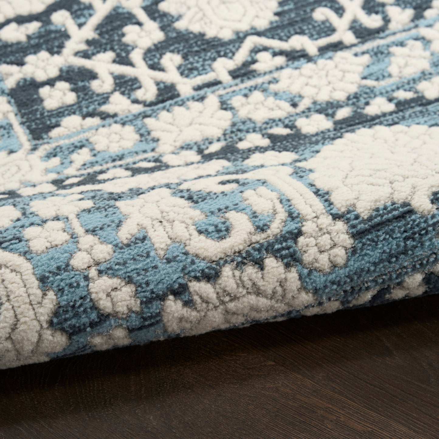 Blue and cream patterned area rug with floral and geometric motifs, plush pile on dark wood floor.