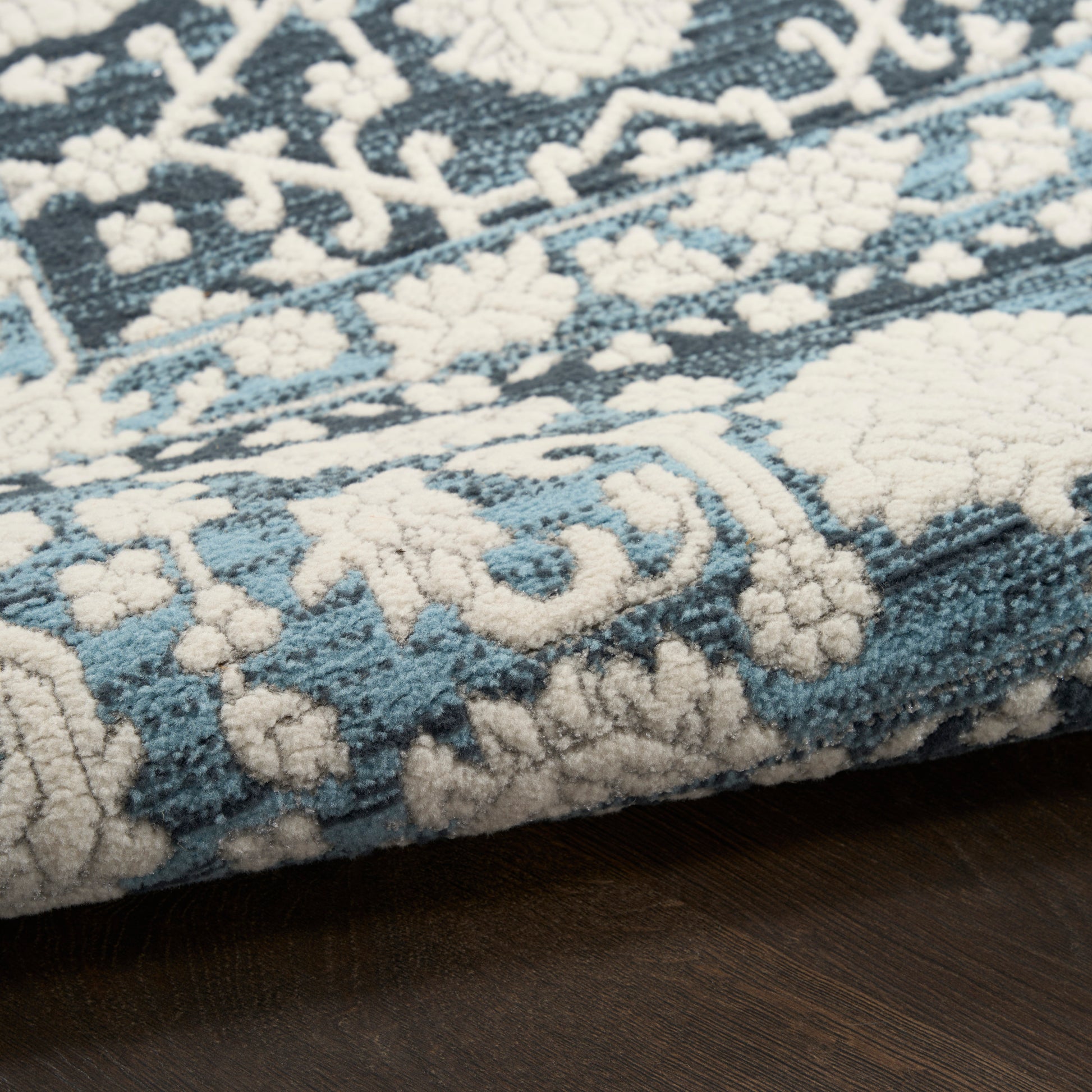 Blue and cream patterned area rug with floral and geometric motifs, plush pile on dark wood floor.