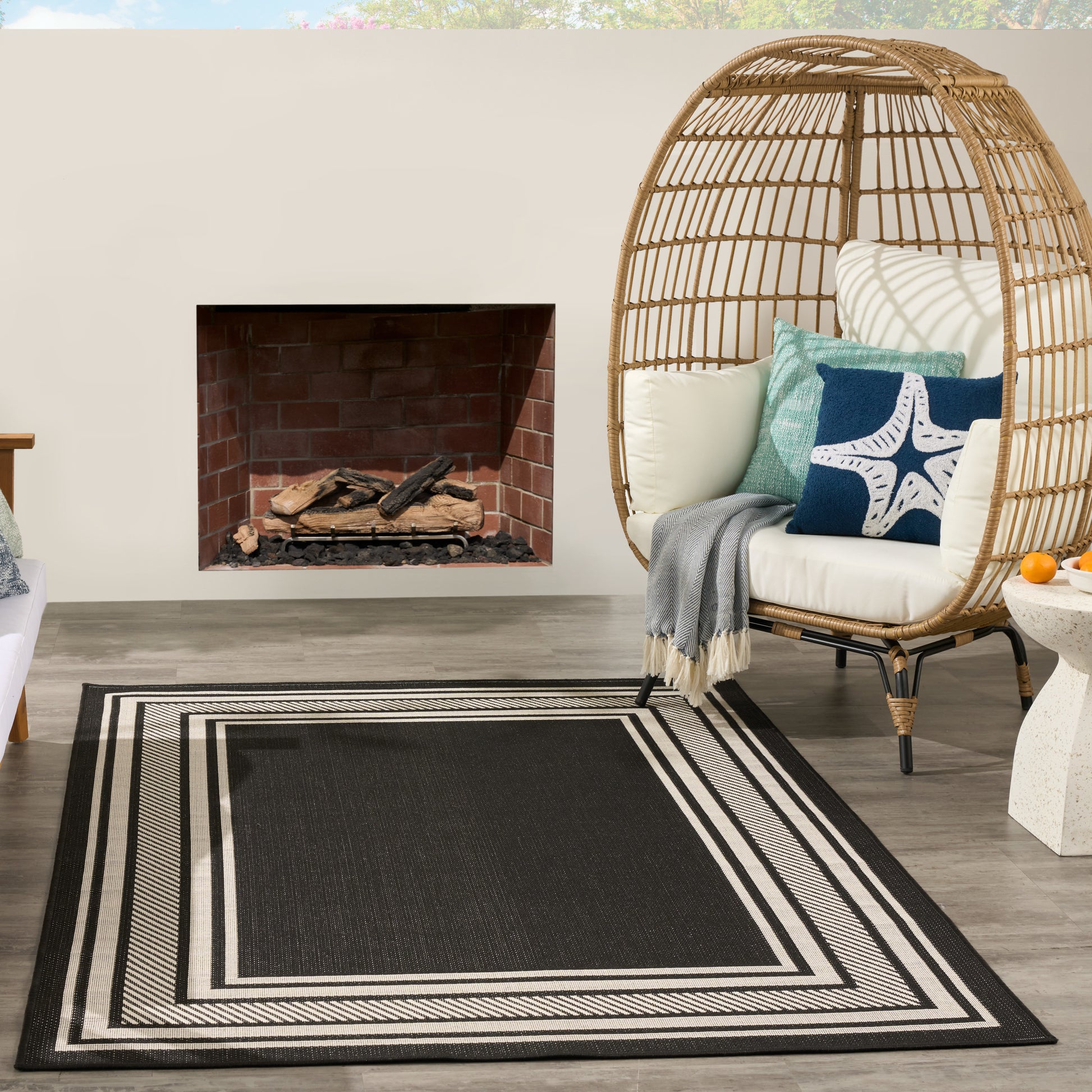 Woven rattan egg chair with light cushions and blue starfish pillow, red brick fireplace, and a black-and-white striped rug.