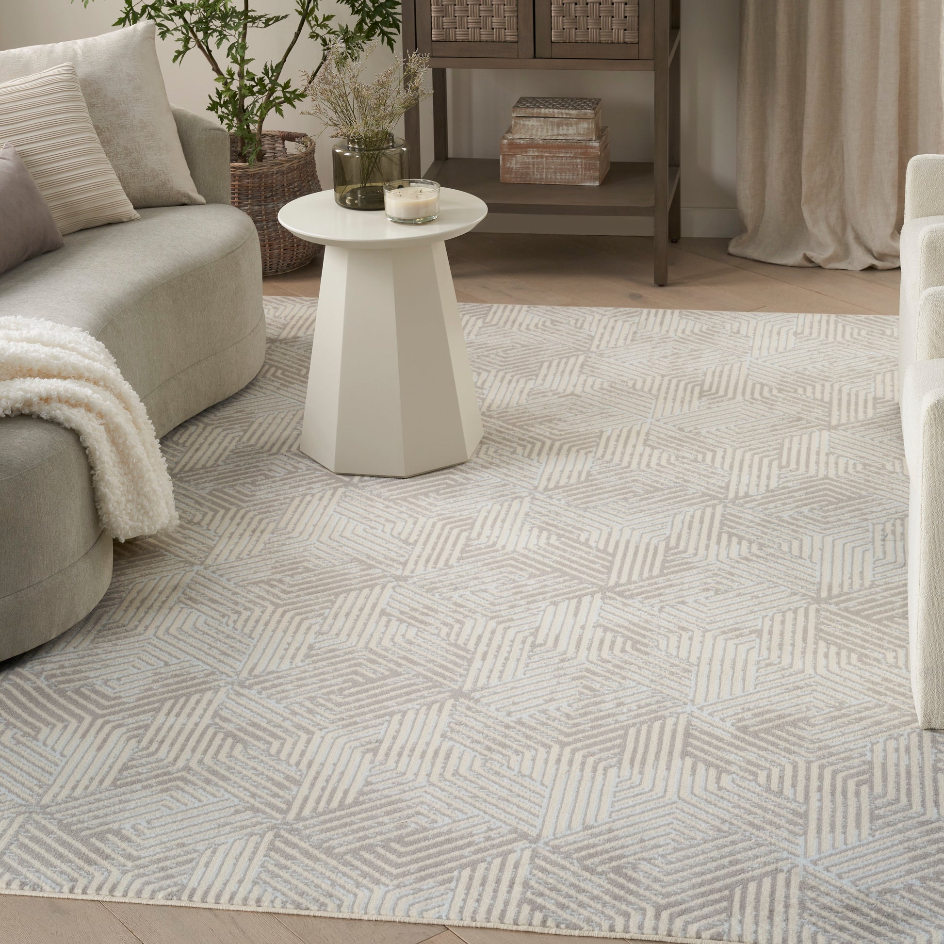 Light beige geometric patterned rug in cream tones; round white pedestal coffee table in a cozy neutral living room.