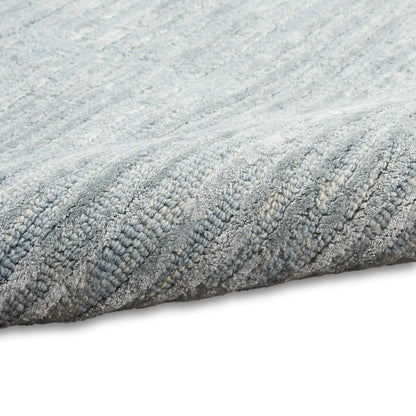 Light gray textured rug with soft loop-pile and subtle diagonal pattern, rolled edge visible.
