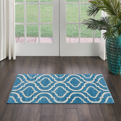Blue rectangular area rug with white interlocking wave pattern in doorway on dark wood floor beside a potted plant.