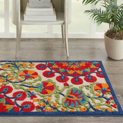 Colorful floral area rug with blue border on wood floor, beside a white shelf with books and a potted plant.
