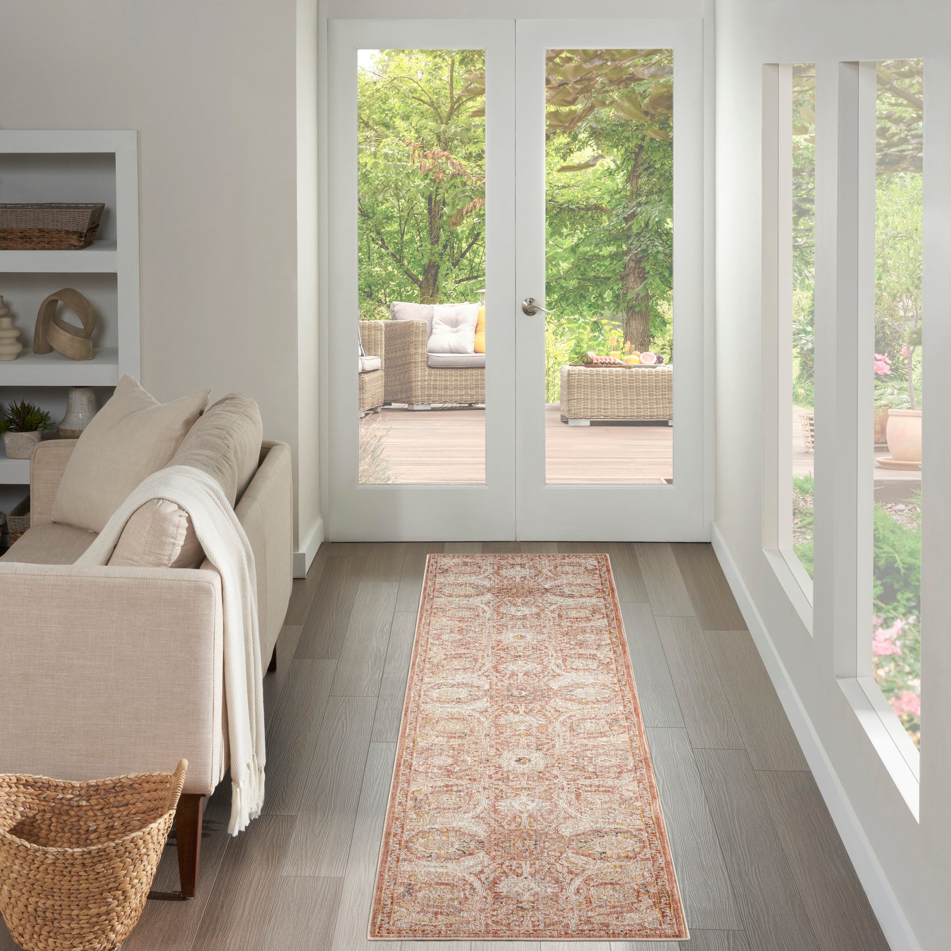 Bright living room with beige sofa, cream throw, white shelves, woven basket; pink-beige oriental runner rug leading to glass doors.