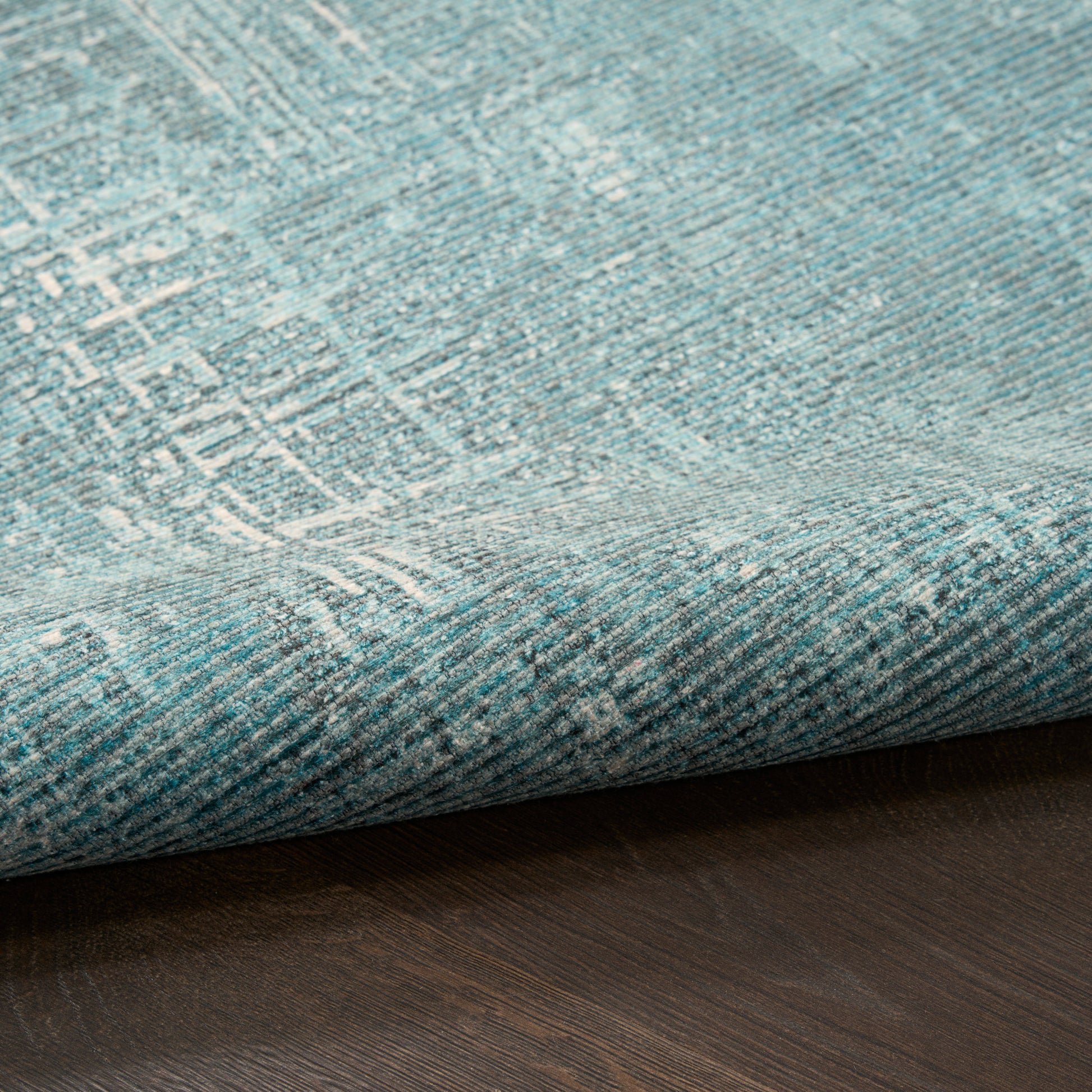 Teal and blue distressed-pattern rug with pale white geometric lines, rolled edge on dark wood floor.