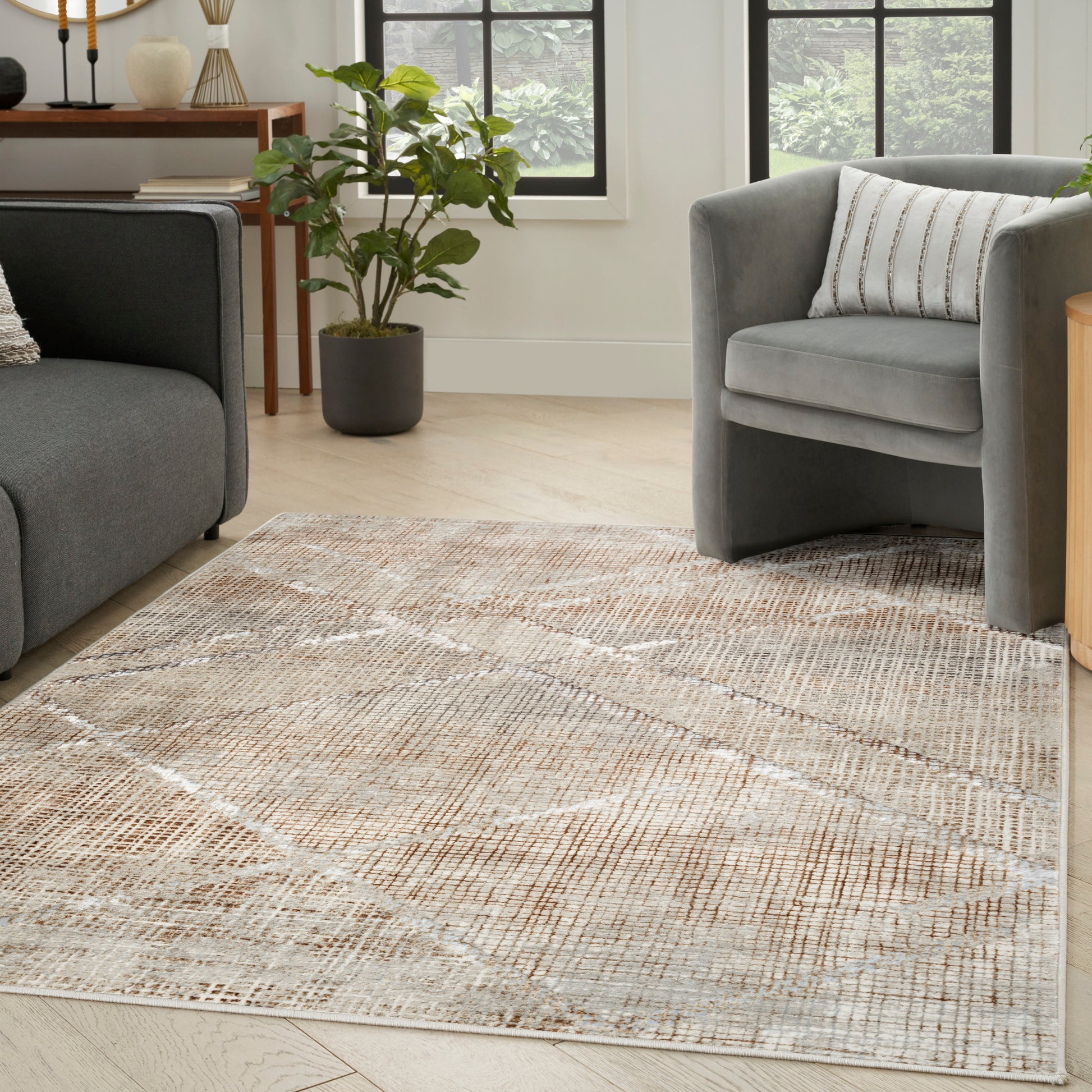 Neutral living room with beige geometric woven rug, gray upholstered sofa and armchair, light wood floor and potted plant.