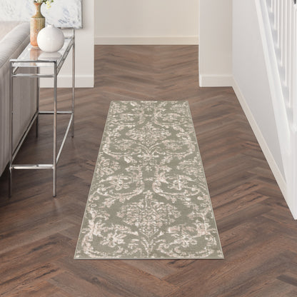 Long damask-patterned runner rug in pale sage and ivory on a dark wood hallway floor, beside a glass-metal console table.
