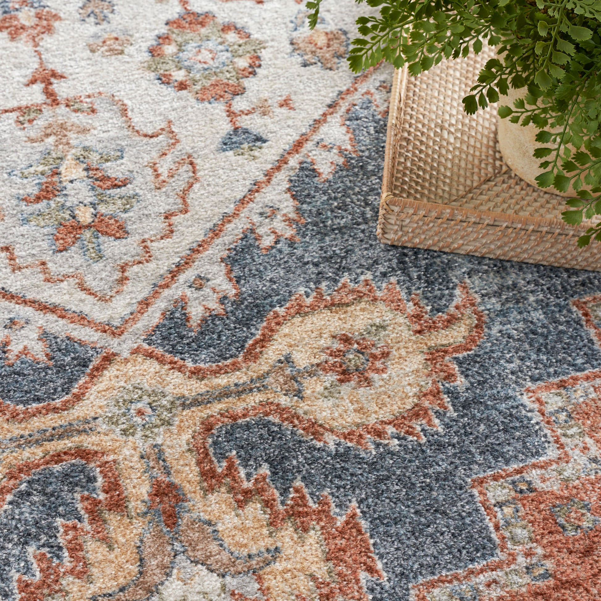 Soft plush oriental rug with ivory, navy and coral floral medallions; wicker basket with greenery nearby.