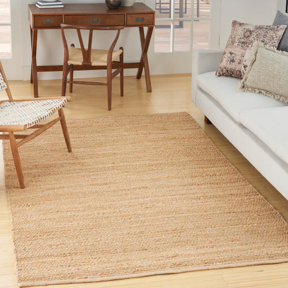 Natural jute area rug in a bright living room with a mid-century desk and chair and a neutral sofa with textured cushions.