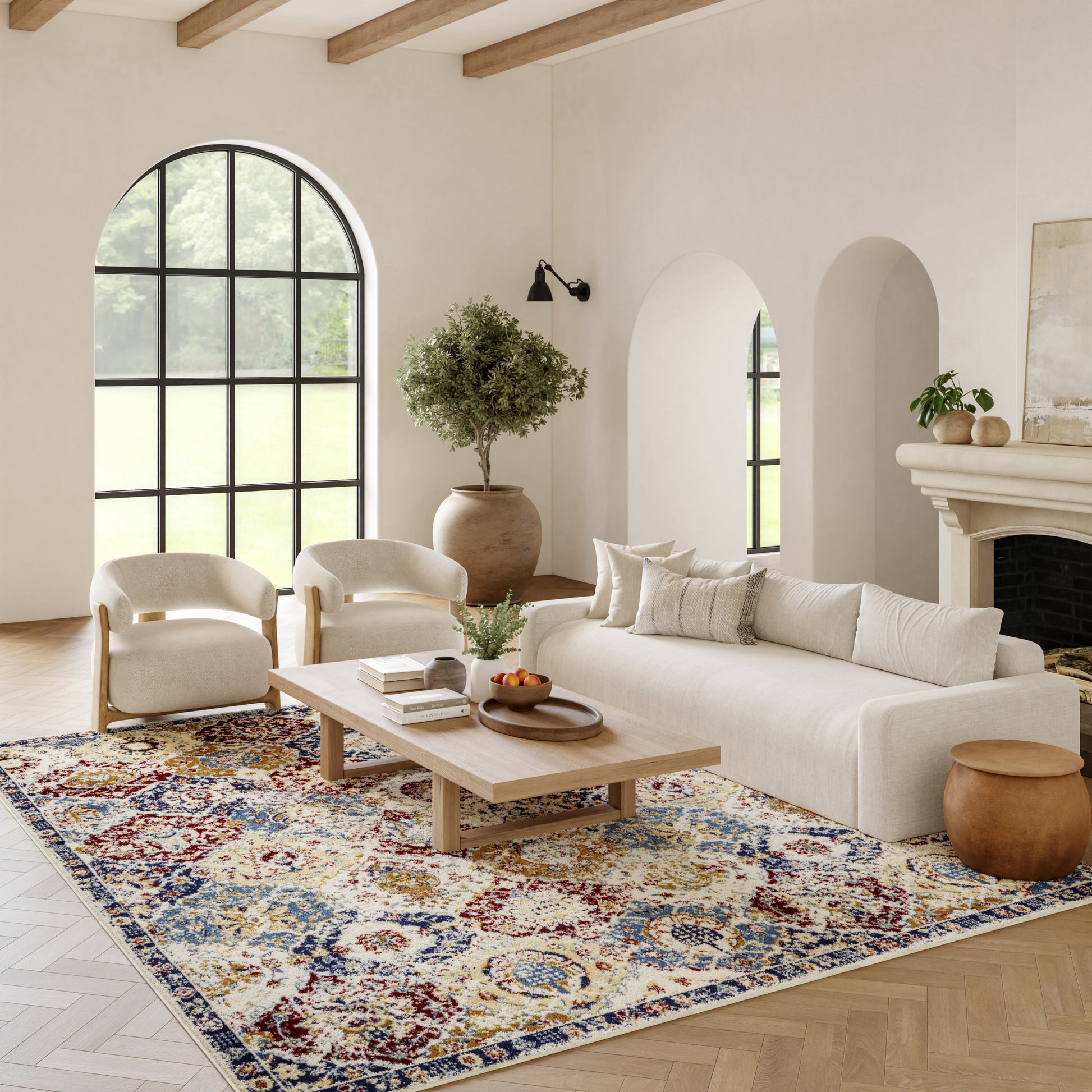 Bright living room with cream sofa and chairs, light wood coffee table, colorful Persian rug, arched windows and doorways, potted plant.