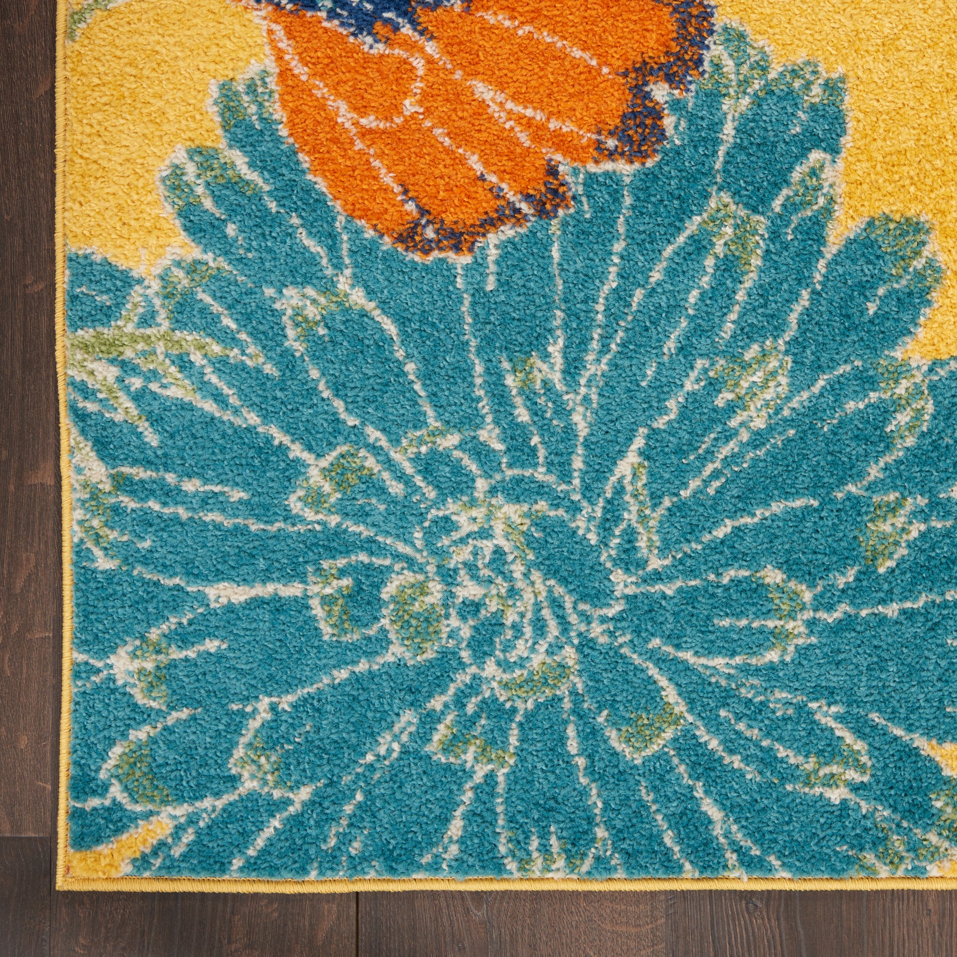 Rectangular tufted area rug with a large blue flower design, orange accent at top, yellow border, on wood floor.