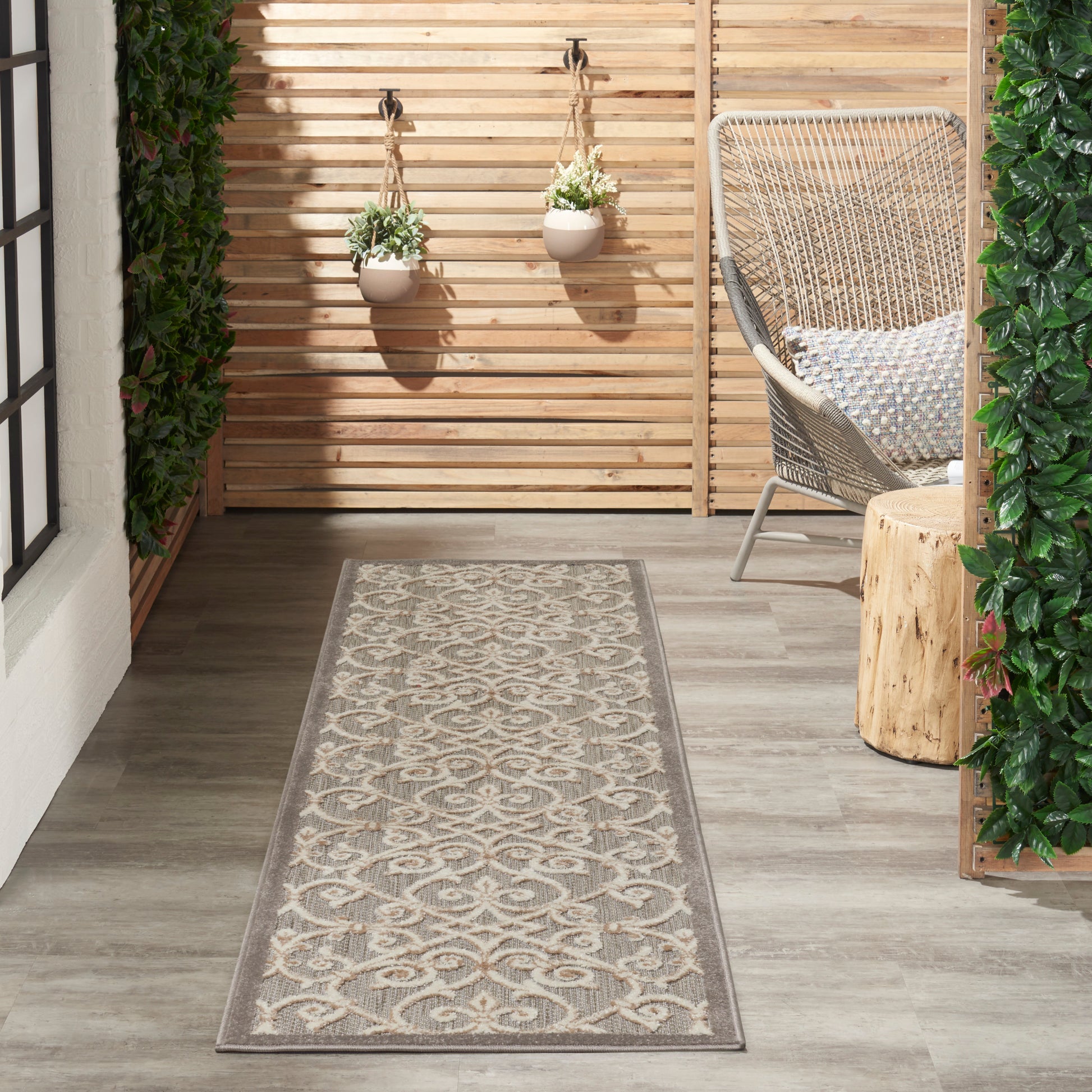 Outdoor rug runner in beige-gray with an ornate pattern on a wooden patio beside a wicker chair.
