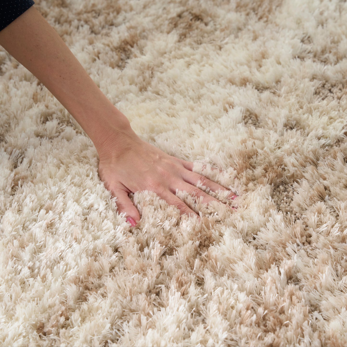 Cream-beige fluffy shag rug with long pile; hand pressing to show plush texture and cozy home decor.