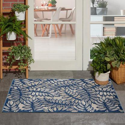 Blue and white fern-leaf patterned rug on a concrete entryway, flanked by plants, leading to a glass door and dining room.