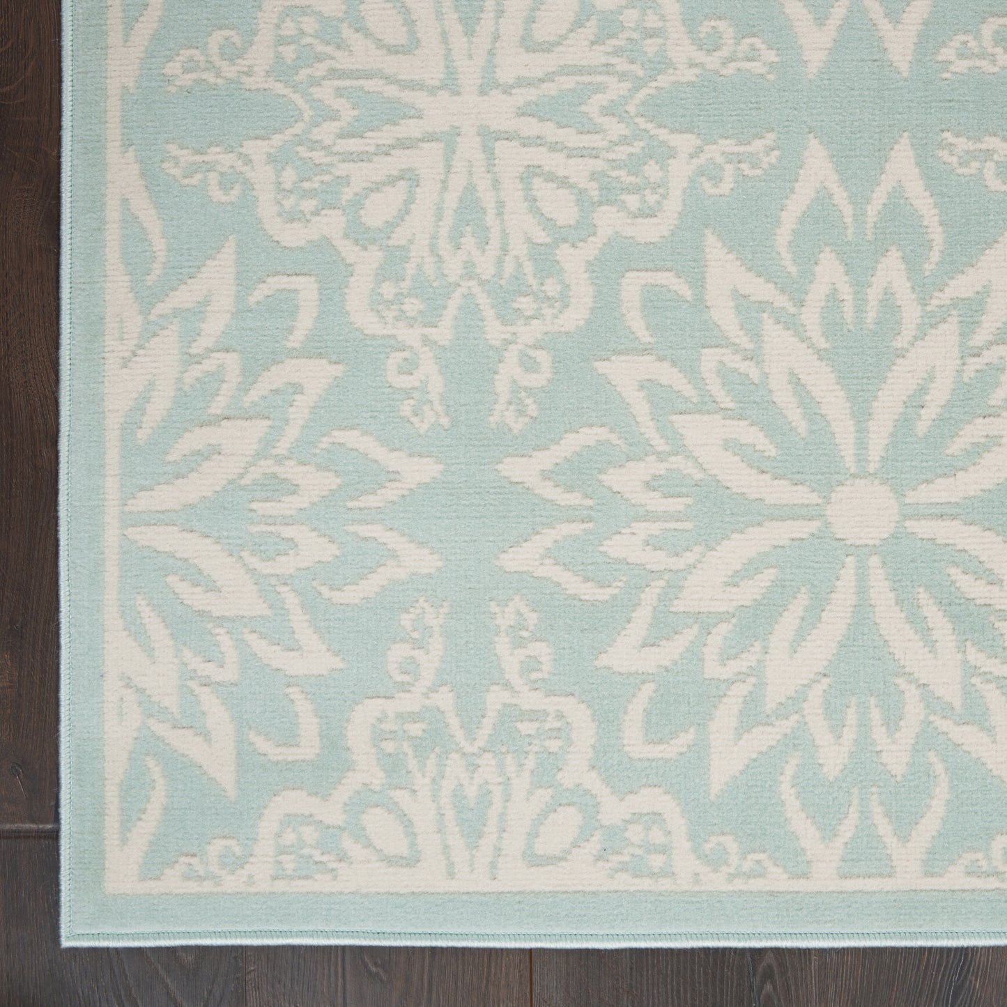 Light blue rug with white damask floral medallion pattern, rectangular with a pale border, on dark wood floor.