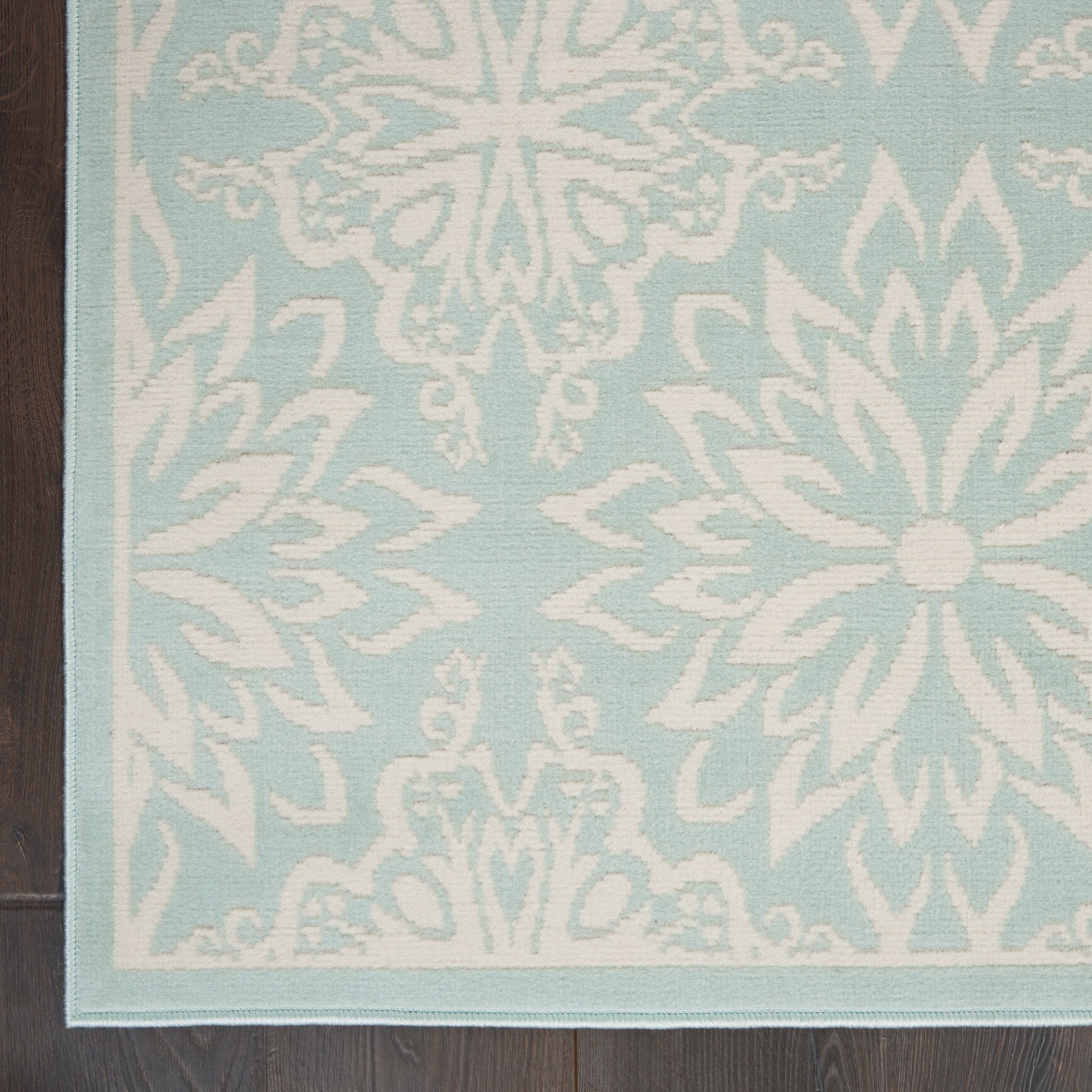 Light blue rug with white damask floral medallion pattern, rectangular with a pale border, on dark wood floor.