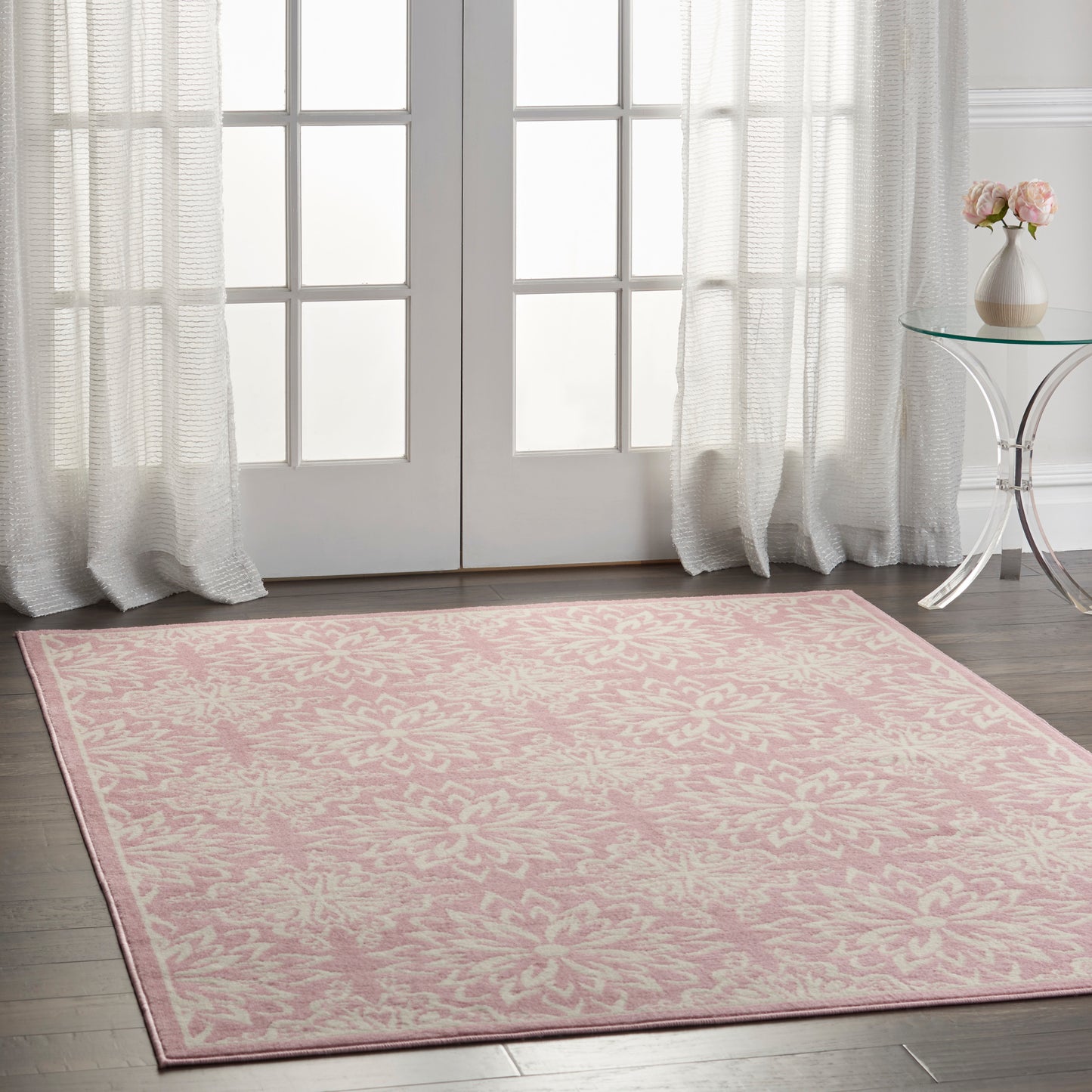 Rectangular pink area rug with white damask floral pattern in a bright room by French doors.