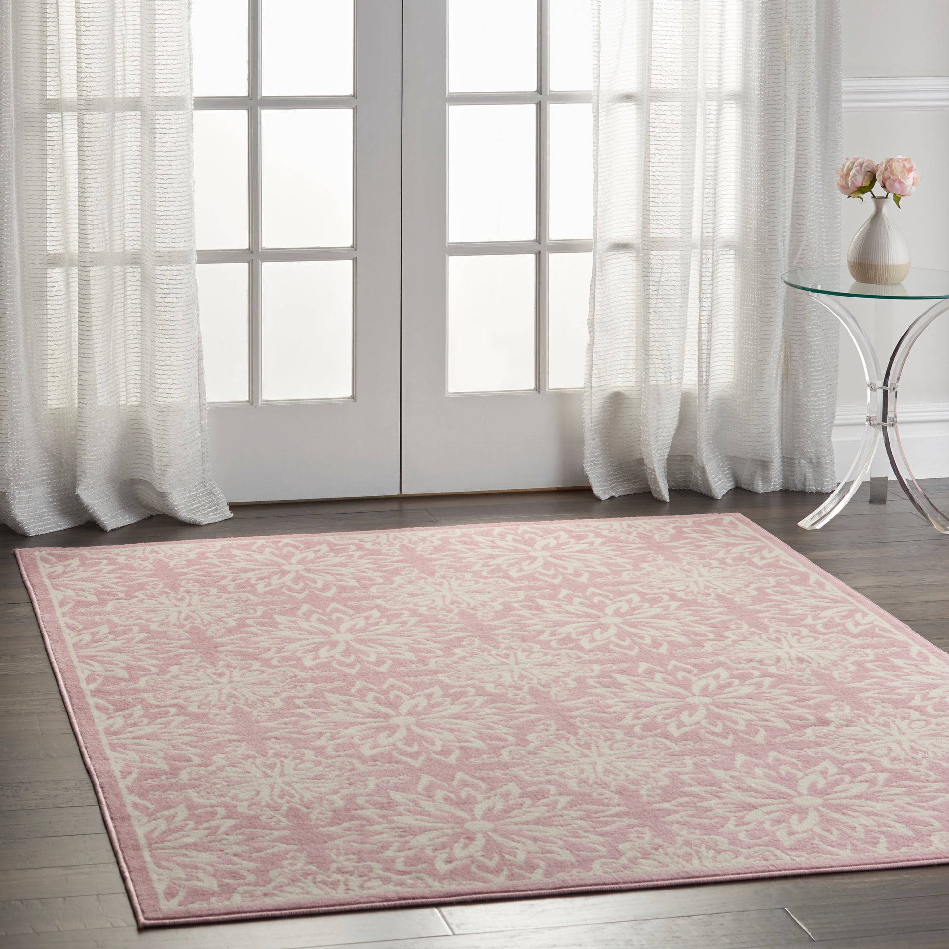 Rectangular pink area rug with white damask floral pattern in a bright room by French doors.