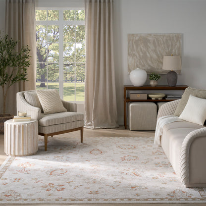 Neutral living room with beige sofa, striped armchair, large window with beige curtains, round wood side table, floral rug, console lamp.