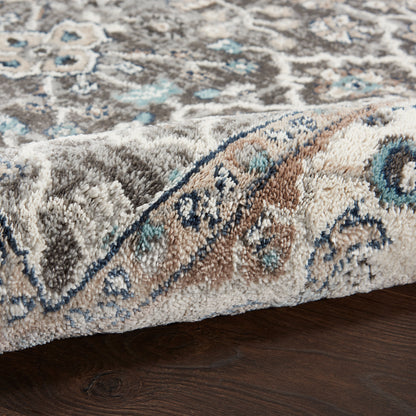 Close-up of a traditional beige-toned rug with blue and teal accents and an ornate border, soft pile on dark wood floor.