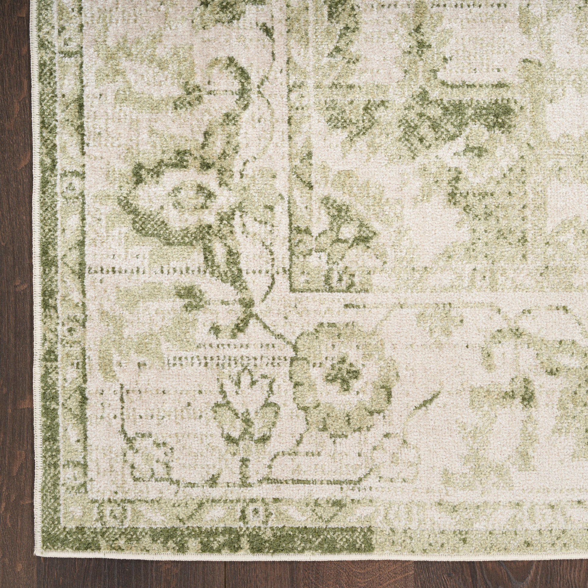Rectangular olive and cream oriental rug with floral border on dark wood floor; fringed edge visible.