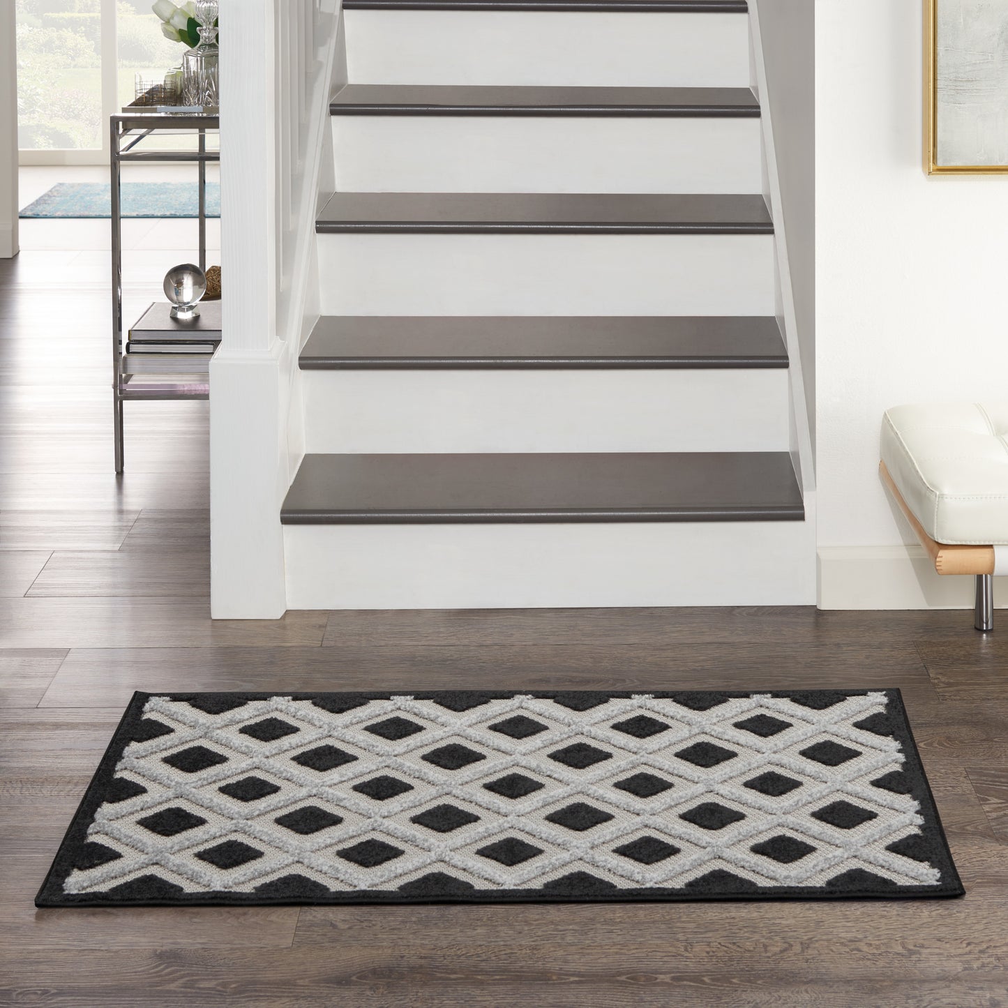 Black-and-white diamond lattice rug with a black border, placed in front of stairs in a modern entryway.