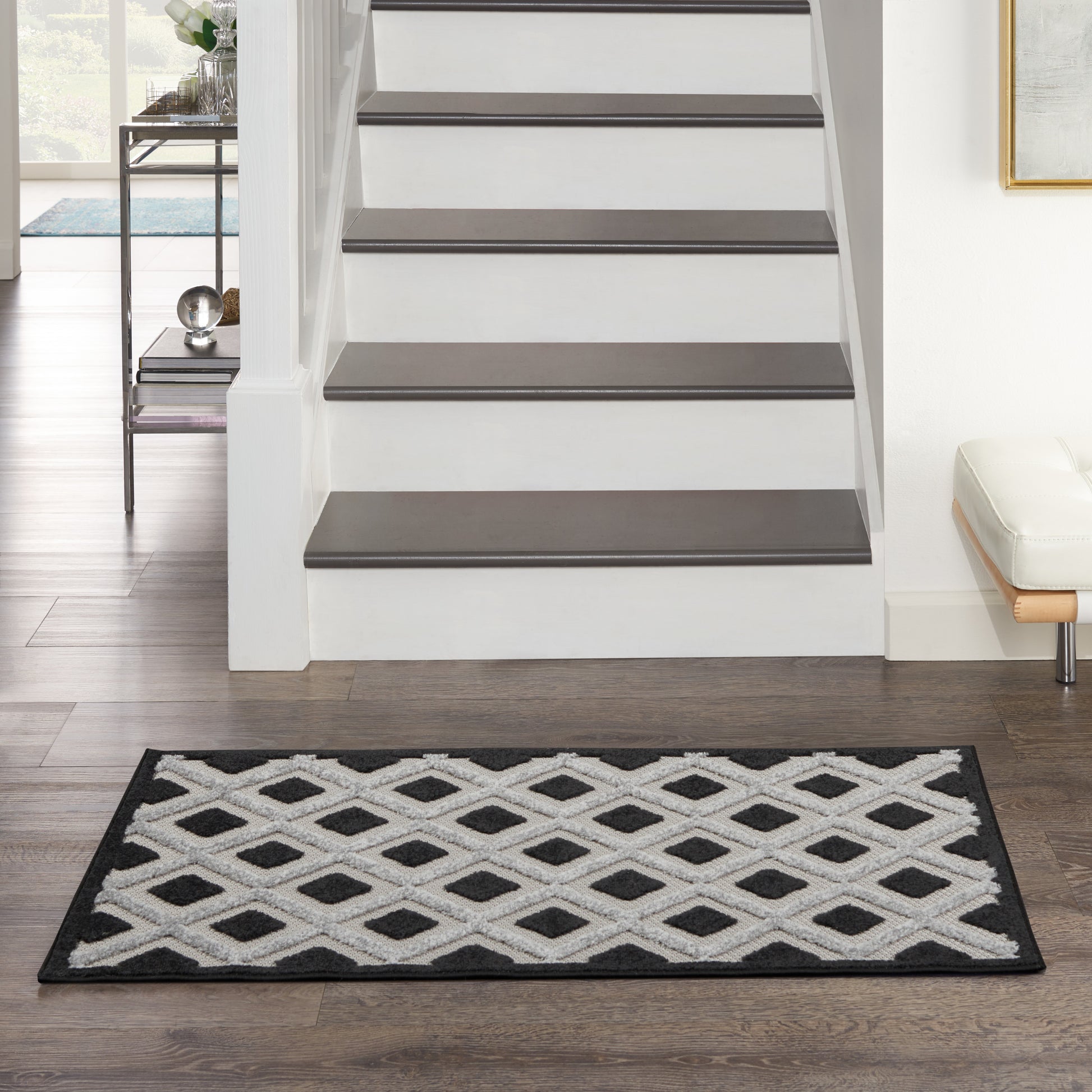 Black-and-white diamond lattice rug with a black border, placed in front of stairs in a modern entryway.